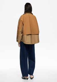 Brązowa i beżowa, warstwowa kurtka z kołnierzem, w oversize'owym fasonie i prążkowanej strukturze, w połączeniu z szerokimi spodniami z ciemnego denimu i szpilkami.