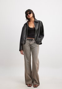 Svart imitationläder jacka med dragkedja över en svart tajt topp, tillsammans med ljusa utsvängda jeans och svarta klacksandaler; accessoriserad med svarta solglasögon.
