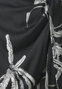 Svart stoff med hvite botaniske trykk, med store bladdesign; glattere tekstur med draperingsdetaljer og en innpakningseffekt.