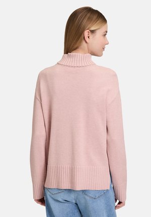 Lichtroze trui met een geribbelde col enzoom. Zachte textuur, verlaagde schouders en een relaxte pasvorm. Ggedragen over blauwe jeans.