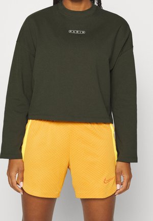 Ciemnozielony, krótki sweatshirt z logiem "PARIS", w zestawieniu z jasno-pomarańczowymi, fakturowanymi szortami z żółtymi akcentami po bokach oraz logo Nike.