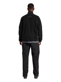 Mand iført sort jakke med lille "ATW" tekst på øvre ryg, sorte bukser og mørke sko, stående med ryggen mod på hvid baggrund.