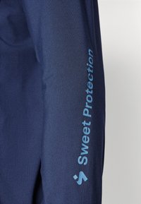 Navyblauwe jacket met een gladde textuur; voorzien van een gedrukt logo in lichtblauw op de linkermouw; aansluitend ontwerp met minimale details.