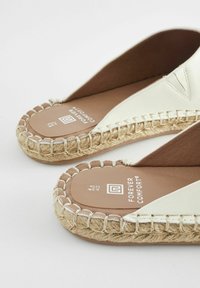 Vita espadrillestil sandaler med en vävd jutebas, bruna innersulor och dekorativ sömnad längs kanterna. Varumärke synligt på sulorna.