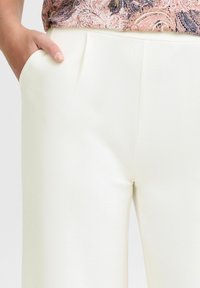 Pantalons blancs taillés avec une texture lisse et un design à jambes droites, comportant des poches latérales et des plis subtils pour un détail supplémentaire.
