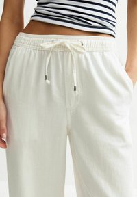 Witte lichtgewicht trainingsbroek met een elastische tailleband en trekkoord, voorzien van zilverkleurige hardware en zijzakken. Gladde textuur.