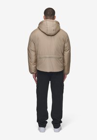 Beige dunjakke med hette, med en glidelåslomme bak, båret med svarte cargo-bukser og hvite sneakers.