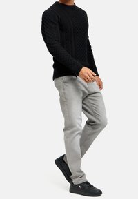 Zwarte gebreide trui met textuurpatronen, gecombineerd met lichtgrijze jeans en zwarte sneakers. Het ontwerp heeft een ronde hals en een slim fit.