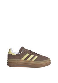 Brown suede Adidas Gazelle sneaker with yellow stripes, yellow heel tab, and thick translucent gum sole.