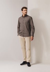 Grijs overhemd met lange mouwen en knopen, voorzien van een borstzak, gecombineerd met beige broek en zwarte sneakers. Eenvoudig ontwerp en een aansluitend silhouet.