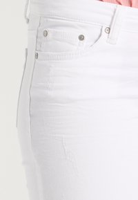 Pantalones vaqueros blancos de mezclilla con un diseño ajustado, que presentan herrajes plateados, bolsillos delanteros y detalles sutiles desgastados a lo largo de la tela.