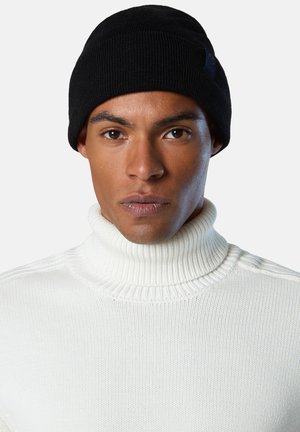 Black knitted beanie worn with a white ribbed turtleneck sweater, featuring a textured design and close-fitting shape.