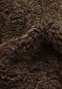 Tissu texturé bouclé marron foncé avec des fibres douces et denses, semblables à de la laine, formant des plis de surface inégaux et moelleux.