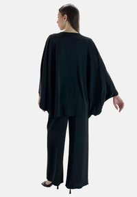 Schwarzes, locker sitzendes Oberteil mit langen Ärmeln, kombiniert mit weit geschnittenen Hosen. Glatte, leichte Stoffqualität mit fließendem Design. Keine sichtbaren Muster oder Beschläge.
