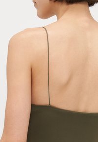 Top verde oliva senza schienale con spalline sottili. Tessuto morbido e design minimalista, con scollatura dritta e silhouette aderente.
