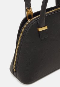 Sac à main en cuir noir texturé avec fermeture éclair dorée, fermoir en métal doré et deux poignées robustes, présenté sur un fond blanc.