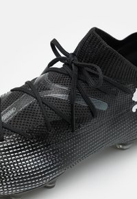 Scarpa sportiva nera con una tomaia in mesh testurizzato, dotata di lacci intrecciati, suola in gomma con motivo e sottili accenti riflettenti.