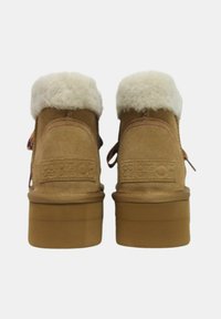 Stivaletti alla caviglia in suede color tan con un morbido risvolto in pelliccia sintetica bianca, dotati di una suola in gomma spessa e lacci colorati con motivo. Logo del marchio impresso sul tallone.