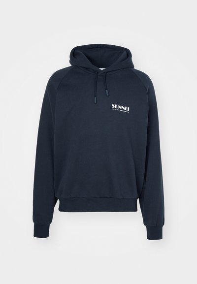Haut à capuche bleu marine foncé avec une poche kangourou, un cordon de serrage réglable et un logo "SUNNEI" blanc sur la poitrine. Tissu doux en coton avec des poignets côtelés.