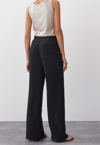 Mustat, leveät housut, joissa on sileä pinta, joustava vyötärö ja takatasku. Yhdistetty kevyen, hihattoman metallivärisen toppin kanssa.