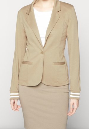 Beige aansluitende blazer met enkele knoopsluiting, witte gestreepte manchetten, gecombineerd met een bijpassende kokerrok en een wit shirtje eronder.