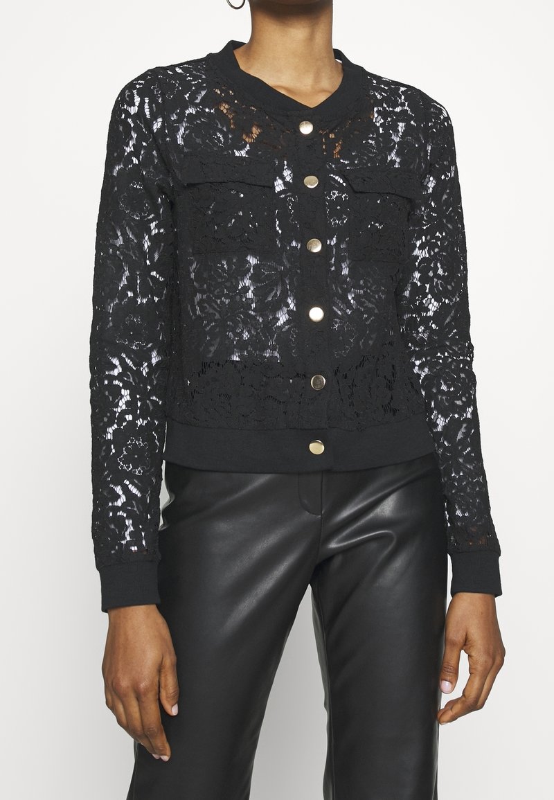 Musta pitsinen bomber-takki, jossa on pitkät hihat, neppari-napit ja ribbaatut hihansuut, hienostuneella kukkakuviolla ja lyhyellä designilla.