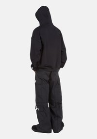 Sweat à capuche noir avec une coupe ample, associé à un pantalon cargo noir avec de grandes poches et des accents de logo blancs.
