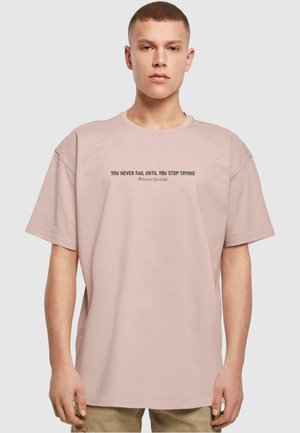T-shirt en coton rose clair à manches courtes avec un texte noir : "VOUS NE RATEZ JAMAIS TANT QUE VOUS CONTINUEZ À ESSAYER #NeverGiveUp." Conception décontractée.