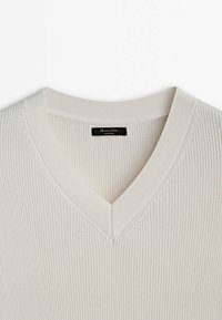 V-neck sweater in light beige, featuring ribbed texture. The collar is wide, with a tag inside marked "Made in China."