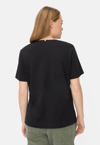Sort bomulds T-shirt med korte ærmer, rund halsudskæring og en lille detalje bagpå. Teksturen ser glat og blød ud.