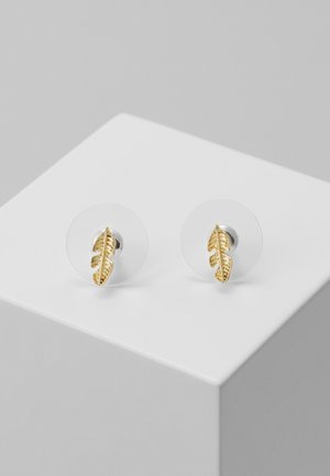 Paire de petites boucles d'oreilles clous en forme de plume dorée avec des attaches rondes transparentes, présentée sur un socle blanc.