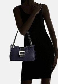 Marinblå handväska i texturerat läder, med en central svart rem och silverdetaljer, kompletterad med dubbla axelremmar.