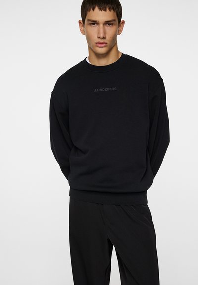 Sort crewneck sweatshirt med en afslappet pasform, lavet af bomuld. Har et subtilt logo foran og ribbede mansjetter. Båret med matchende sorte bukser.