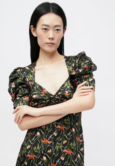 Robe florale avec un fond noir, dotée de manches bouffantes et d'un détail frontal torsadé. Motifs floraux verts et rouges tout au long.