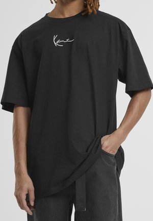 Schwarzes Baumwoll-T-Shirt mit lockerem Schnitt, kurzen Ärmeln und einem weißen Signaturlogo auf der Brust. Glatte Textur und minimalistisches Design.