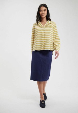 Blouse rayée jaune et blanche avec un col ; associée à une jupe bleu marine longueur genou. Design simple, tissu léger, coupe décontractée.
