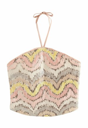 Jonge vrouw met lang blond haar, die een strapless jurk met pailletten draagt met roze, gele en beige golvende patronen tegen een lichte achtergrond.