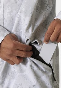 Voděodolná bunda v světle šedé barvě s texturovaným vzorem. Obsahuje kapsu na zip, do které je zasouvána karta.