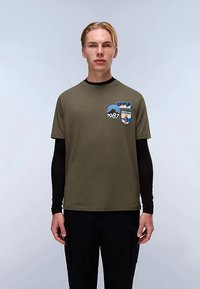 Oliwkowa koszulka z krótkim rękawem i okrągłym dekoltem, z niebieską grafiką góry w kształcie koła oraz naszywkami "Napoli" i "1987".