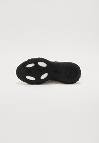 Schwarze Sneaker-Sohle mit strukturierten Rillen, runden weißen Akzenten und ovalen Aussparungen. Das Markenlogo ist auf der Oberflächen der Sohle sichtbar.