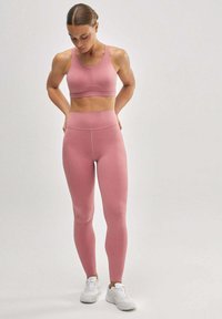 Sujetador deportivo rosa claro y leggins a juego, hechos de una tela elástica. Zapatillas deportivas blancas. Textura suave, diseño ajustado.