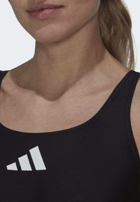 Black athletic tank top featuring a white logo design on the left side. Smooth texture and wide straps at the shoulders.