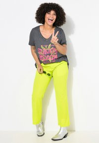 T-shirt gris en V avec un graphique coloré "Sunny Beach", associé à un pantalon droit néon jaune vif et des bottines argentées brillantes.