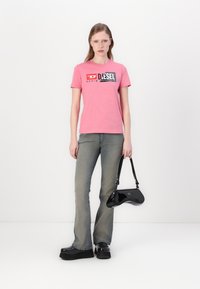 Pink cotton t-shirt with black logo, gray flared jeans, and black patent handbag. Black platform shoes with wide soles. Neutral background.