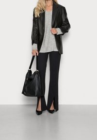 Blazer en cuir noir, pull en maille gris, pantalons évasés noirs avec fentes à l'avant, et un grand sac fourre-tout noir. Des escarpins noirs à bouts pointus complètent la tenue.