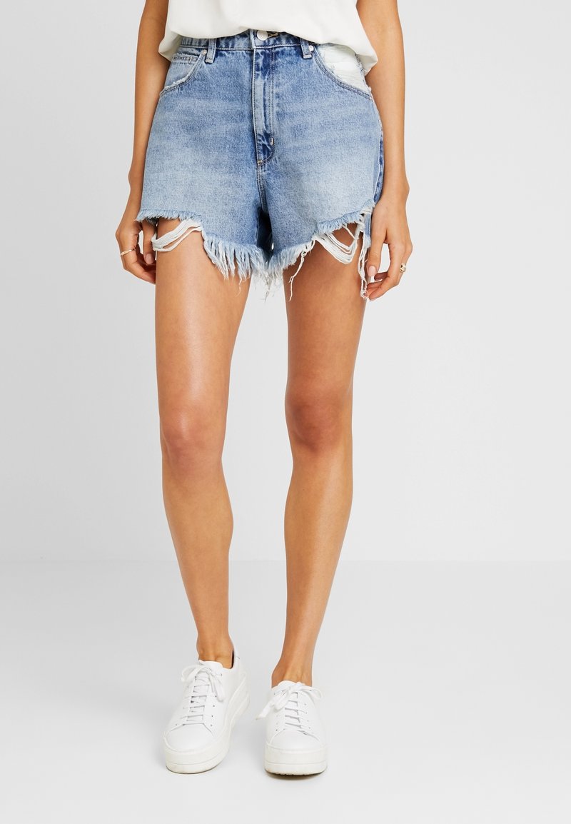 Světle modré džínové šortky s třepeným lemem, vysokým pasem a ošoupanými detaily. Kombinovány s bílými teniskami.