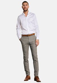 Weißes langärmeliges Hemd mit Stehkragen, kombiniert mit hellgrauen karierten Hosen und braunen Lederschuhen, ergänzt durch einen braunen Ledergürtel.