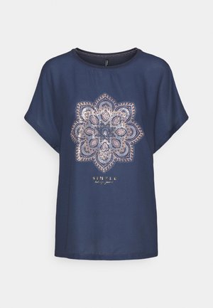 Granatowa koszula z krótkim rękawem z dużym, skomplikowanym wzorem mandali w beżowych i białych cekinach oraz napisem "PROSTE, ale znaczące" pod spodem.