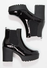 Černé kotníkové boty z lakované kůže s robustním podpatkem, elastickými bočními panely a texturovanou gumovou podrážkou pro lepší přilnavost. Mají praktickou poutko pro snadné nazouvání.