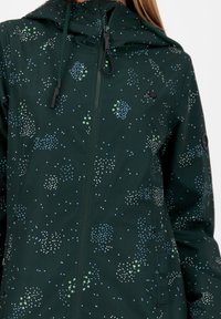 Groene waterdichte jas met capuchon, voorzien van een stippenpatroon in wit, blauw en groen. Gestructureerde stof en ritssluiting aan de voorkant.